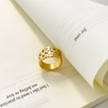 Nahaufnahme eines vergoldeten Titanrings mit unregelmäßiger Schuppenstruktur auf Buch - US 6 / Blatt