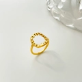 Détail d'une bague florale dorée ajourée irrégulière sur un fond gris clair minimaliste - Plantes évidées