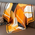 Détail d'un carré de soie aux motifs géométriques orange sur une surface en cuir - Orange