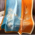 Floral print oversized silk scarf in vibrant orange and sky blue draped on a leather couch - 90*180cm / Light Blue Orange