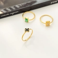 Dettaglio di tre anelli in oro 18K con zircone verde, pietra chiara e motivo a croce - US 6 / Croce Nera