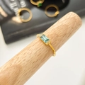 Dettaglio macro di anello dorato con zircone verde rettangolare e pietre laterali - US 6 / Zirconia Blu-Verde con Accenti