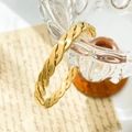 Macro detail van gouden gedraaide open armband hangend aan een decoratief glas - Gevlochten Kruis (Goud)