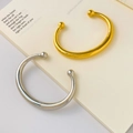 Detailed view of minimalist gold and silver cuff bangles on an open book background - Hollow Arc Double Ball Gold