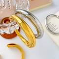 Close-up of polished 18K gold and silver hollow geometric bangles on glass - Gradient Thickness Open Hollow Gold