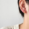 Close-up of golden hoop earring with a round turquoise pendant worn by a model - Mini Blue Zirconia