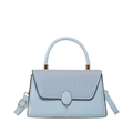 Bolso azul claro minimalista con solapa tejida y herrajes dorados sobre fondo blanco - Azul