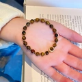Tiger eye natural stone beaded bracelet with golden charm shown on a soft book background - Tiger Eye Micro-Inlaid Zirconia Round Pendant Style
