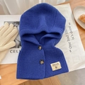 Close-up of blue knitted balaclava with two buttons and label on a wooden surface - Klein Blue