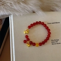 Dettaglio del bracciale in agata rossa con ciondoli Pixiu e zucca dorati su un libro - Stile Cavallo della Fortuna Zucca (C474)