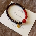 Detalle macro de pulsera de cuentas de granate con colgante dorado sobre tarjeta vintage - Granate Empalmado Con Ágata Roja del Sur Colgante Fu (C377)