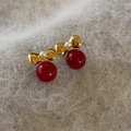 Primer plano de pendientes festivos de perlas rojas con lazos dorados en tela de felpa - Lazo Dorado Perla Roja