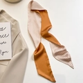 Detalle de un pañuelo twilly de satén naranja caramelo con estampado de pata de gallo - 100cmx8cm / Grulla de Papel Naranja