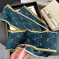 Nahaufnahme des dunkelgrünen Seidenschals mit goldenem Kettenmuster auf einer Handtasche - Pfauenblau
