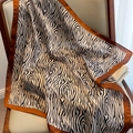 Elegante pañuelo de seda con estampado de cebra y borde café sobre una silla de madera - Cebra Café