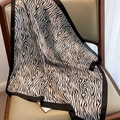 Detalle de pañuelo de seda con estampado de cebra y borde de satén negro en silla cuero - Estampado de Cebra Beige Negro