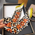 Dettaglio di sciarpa in seta leopardata con lettere arancioni vicino a borsa in pelle - Bordo Giallo