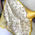 Elegant cream floral silk square scarf with yellow borders draped on a modern grey sofa - Small Floral Creamy Yellow