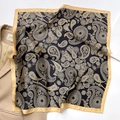 Primer plano de pañuelo de seda paisley negro y dorado sobre una chaqueta beige - Borde Amarillo