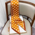 Detailed view of glossy orange polka dot silk scarf draped on a white leather chair - Turmeric