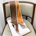 Polka dot skinny silk scarf in orange and brown draped over a leather chair - Yellow Coffee