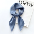 Close-up of deep blue silk square scarf tied in a bow next to a fashion magazine - 65x65cm / Sky Blue