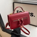 Bolso bandolera rojo oscuro con cremallera doble y borlas largas sostenido a mano - Rojo