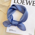 Detailed view of a royal blue silk scarf tied in a bow on a beige shirt with a magazine - 53*53cm / Haze Blue