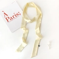 Detail view of a pale yellow satin skinny scarf with smooth texture and a small black label - Beige