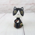 Close-up of a cute black and white resin cat figurine with a dango snack on a wood base - Shaking Head Ornament - Black and White Cat with Dango