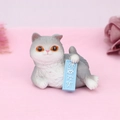 Macro detail of cartoon cat resin ornament with orange eyes holding a blue sign - Fake Smile (1D)
