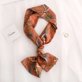 Elegant orange silk twilly scarf with vintage chain print tied in a bow on white fabric - Orange Wheel