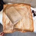 Detailed close-up of leopard print silk scarf with classic Greek key geometric border - Caramel Orange