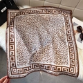 Leopard print silk square scarf with Greek key pattern border on white plush rug - Coffee