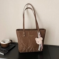Brown leather tote bag with pleated texture and plush bear charm on a studio surface - Brown