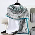 Detail of silk-feel scarf featuring green paisley patterns and satin borders on a hanger - 180x90cm / Cyan