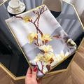Detail van zijdeachtige sjaal met magnolia-print en gele rolzoom op een tafelblad - Zilverijs