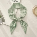 Detail of green floral skinny scarf tied in a bow on a textured linen background - Letter Y (Beige Grass Green Flower)