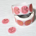 Close-up of round pink Thank You stickers roll with gold foil lettering for packaging - 25mm/500 Stickers / Pink
