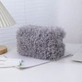 Detailed view of gray plush makeup bag with zipper closure on a white desk with shadows - Gray
