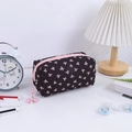 Detailed view of black quilted makeup bag with pink bow print and pearl pendant - Black