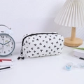 Detail of white bow-patterned makeup bag with pearl pendant on a desk - White