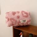 Close-up of pink fuzzy heart makeup bag with lamb wool texture and brand cloth label - Pink