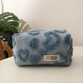 Macro view of plush light blue makeup bag with embroidered dark blue hearts and woven label - Blue