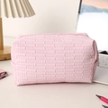 Nahaufnahme der rosa gesteppten Kosmetiktasche mit Webstruktur auf weißem Tisch - Hellrosa