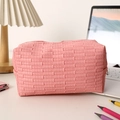 Detailansicht der rosa geflochtenen Kosmetiktasche auf einem Tisch in warmer Atmosphäre - Karminrosa