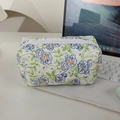 Blumige gesteppte Kosmetiktasche mit blauen Blumen neben einem Laptop auf dem Tisch - Orchidee und Grüne Blätter