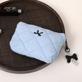 Detail view of a quilted light blue cosmetic bag featuring a cute bow pendant - Blue