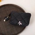 Detailed shot of a black quilted makeup bag featuring pink bow embroidery and pearl charm - Black