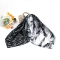 Close-up of black and white palm leaf pattern silk scarf draped over a straw beach bag - Black